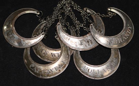 A set of six white metal crescent shaped wine labels.